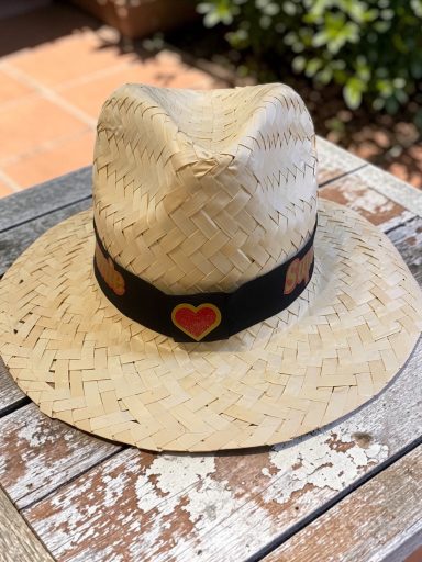 Chapeau personnalisé Chapeau en paille avec un bandeau noir et un cœur en motif, posé sur une table en bois.